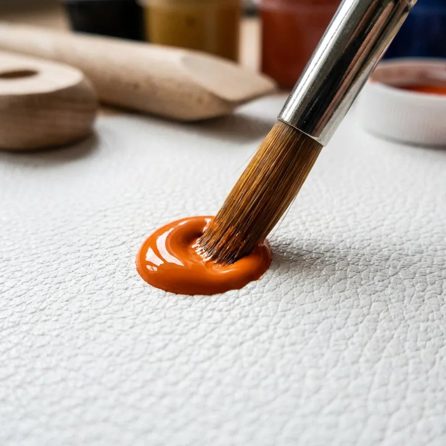 Pinsel berührt orangefarbene Lederfarbe auf einer weißen Oberfläche